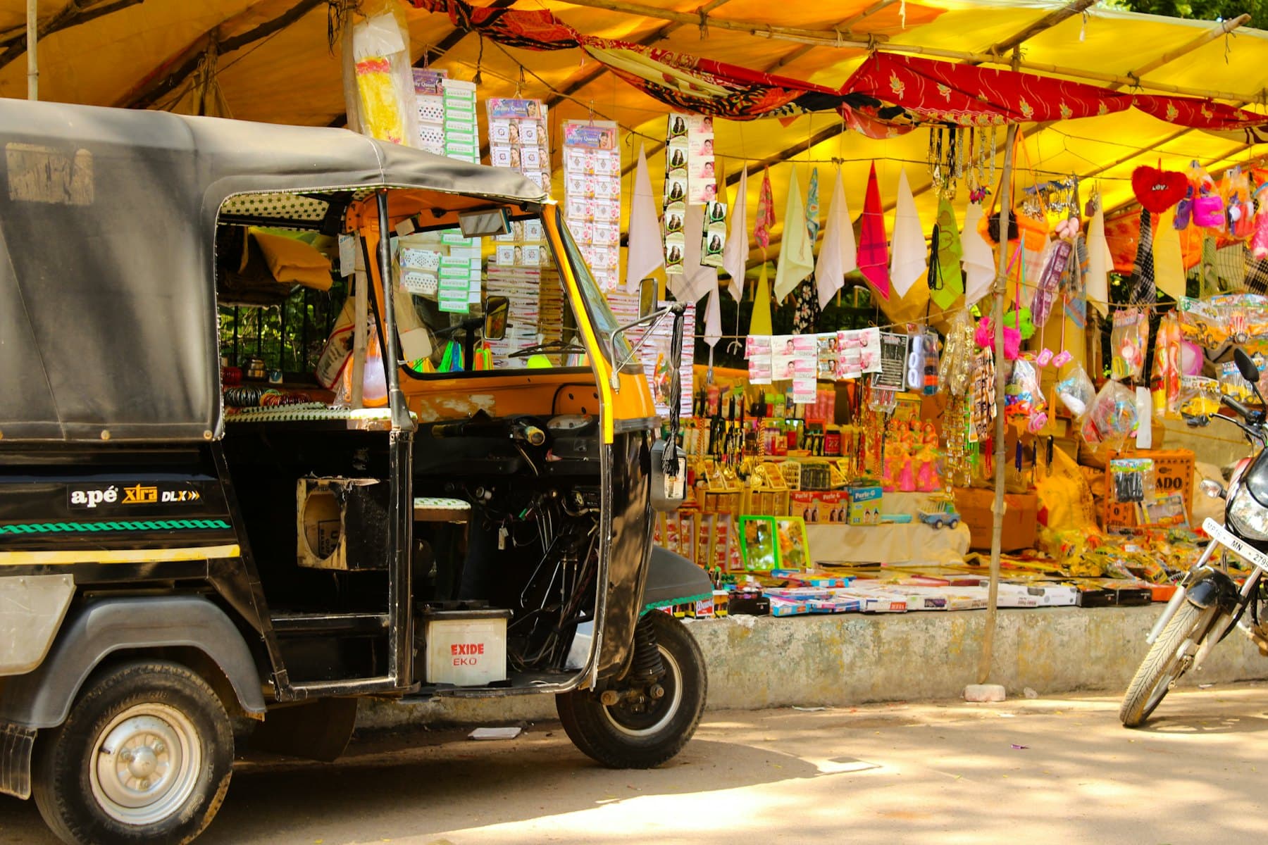 An auto-rickshaw waiting beside a market stall hung with bright goods