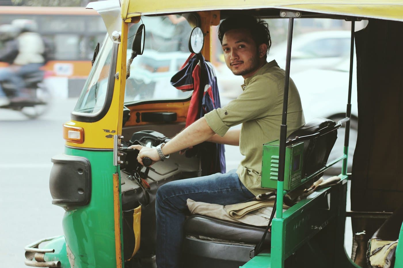 An auto-rickshaw driver smiling at the camera from behind the handlebar